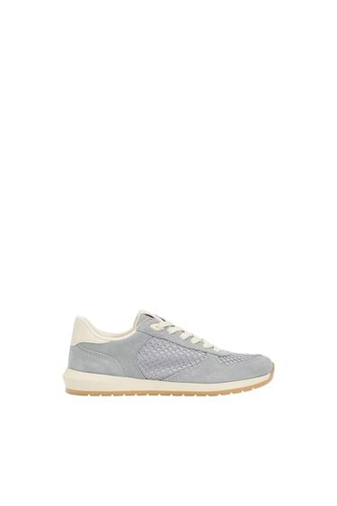 Greyish-blue trainers with braided panels, white laces and rubber soles, profile view on a white background.