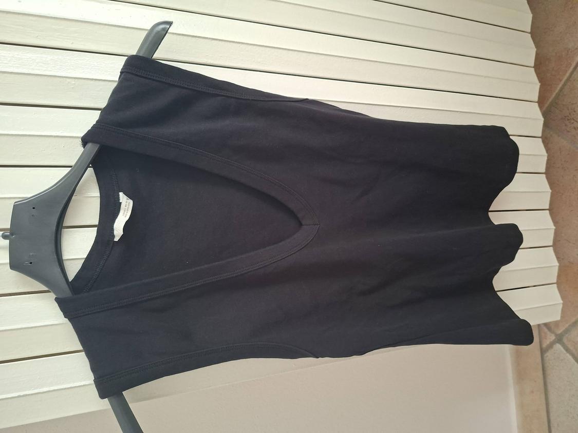 Black sleeveless t-shirt hanging on a black hanger against a white slat background. Label visible inside.