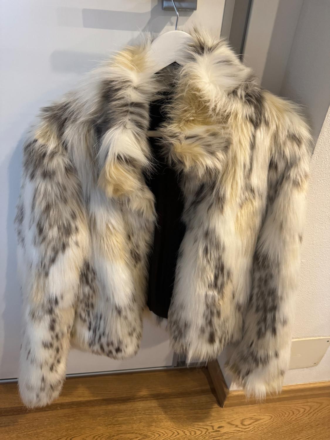 Faux fur coat with mottled print in white, grey, and beige, hanging on a hanger over a wooden floor.