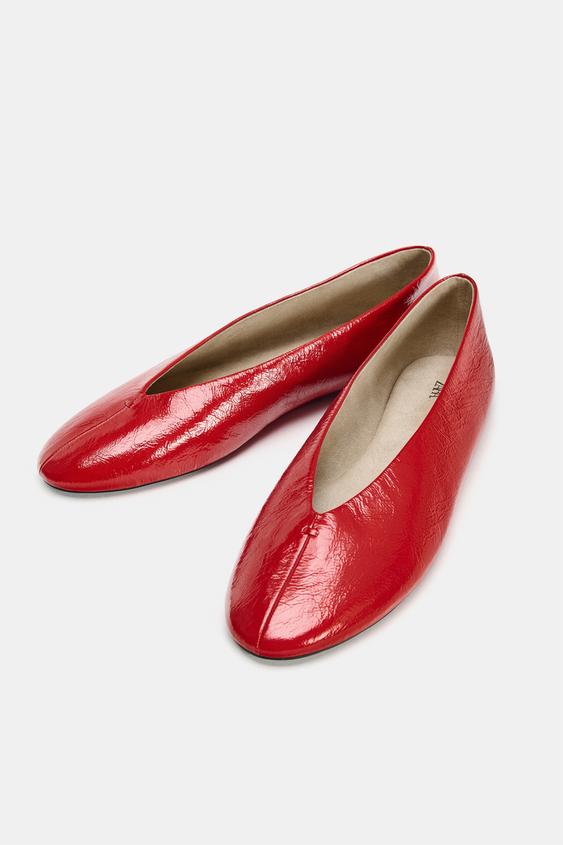 Červené ploché boty s lesklým povrchem a zaoblenou špičkou.