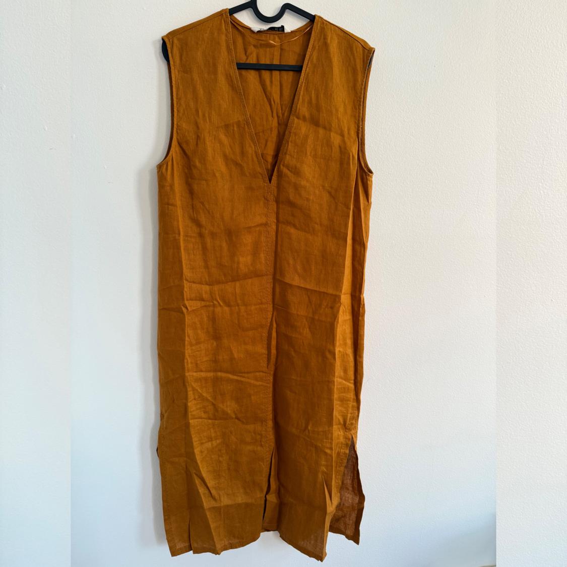 Sleeveless mustard-colored dress with a V-neck, hanging on a hanger against a white wall.