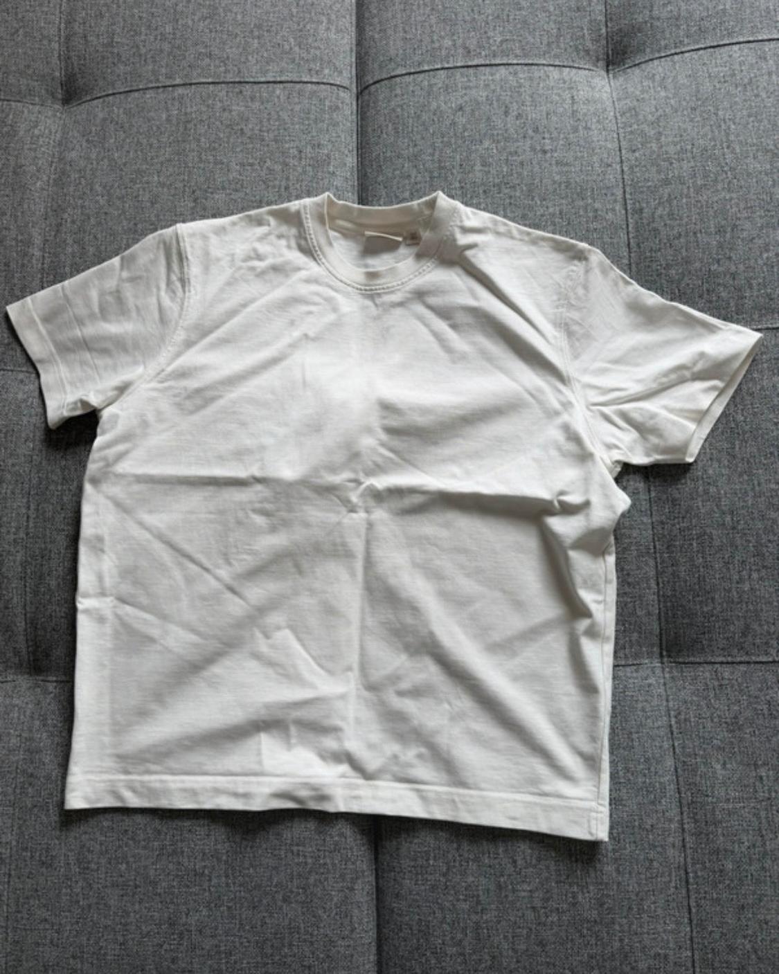 Basic white short-sleeved, crew-neck t-shirt, laid out loosely on a grey fabric sofa with stitching.