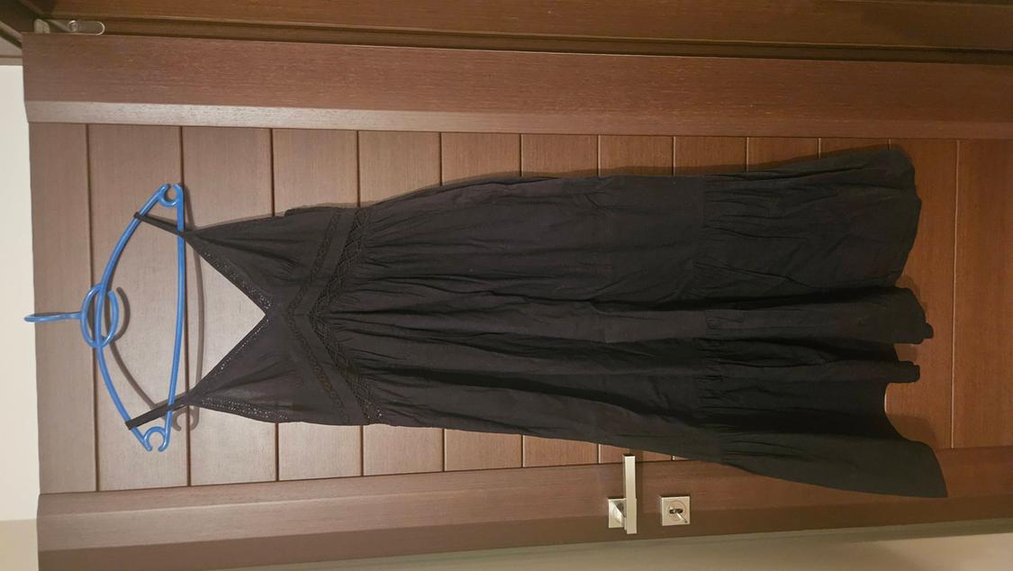 Black dress hanging on a blue hanger over a wooden door. The design is simple and sleeveless.