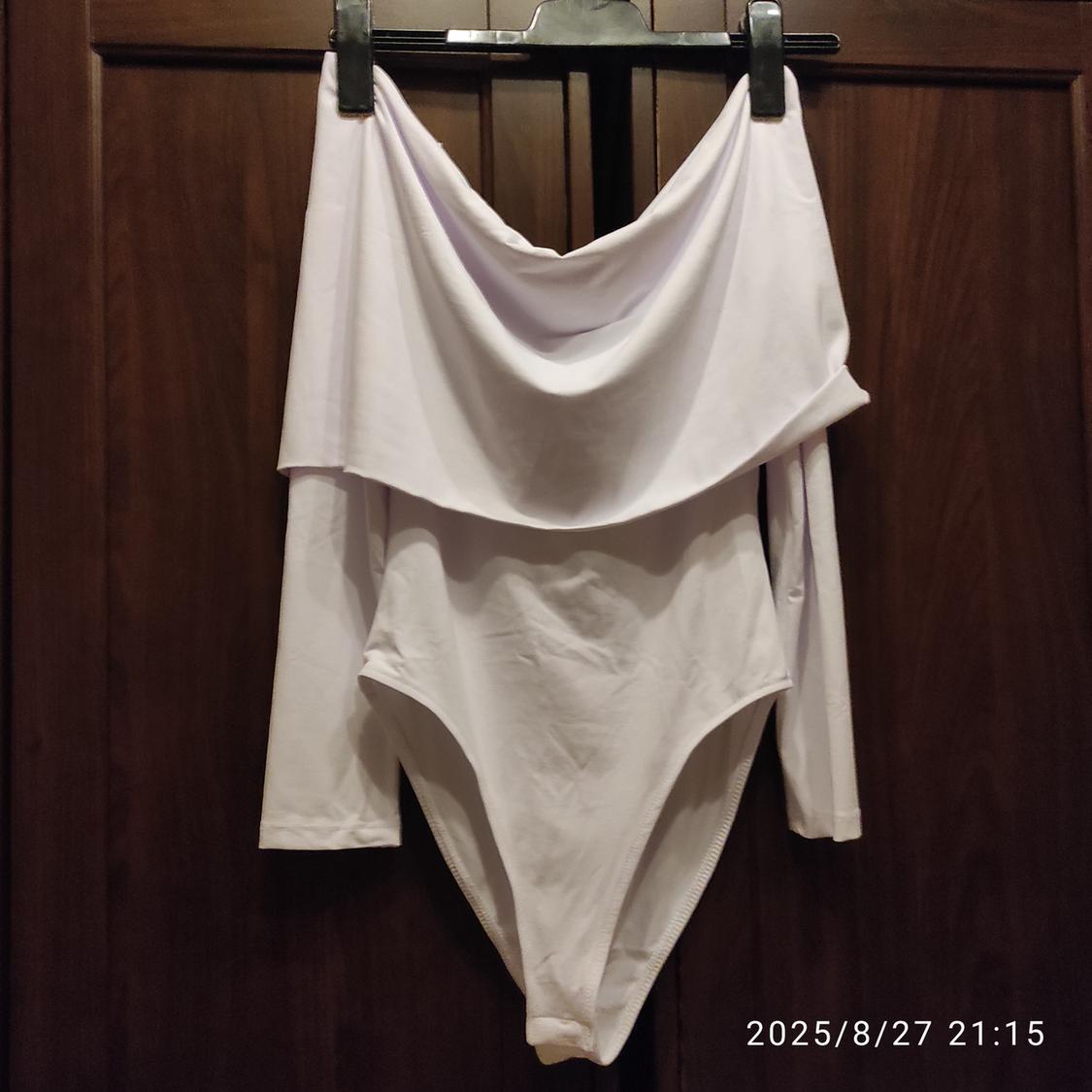 White long-sleeved bodysuit with a draped neckline hanging on a black hanger on a wooden door. Date: 2025/8/27 21:15.