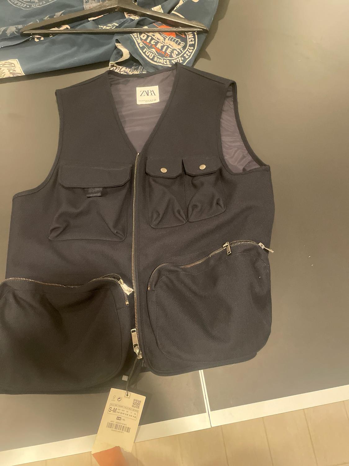 Black vest with pockets and ZARA tag on a gray background. Above, blue garment with text DICKIES SINCE 1922 FORT WORTH, TX.