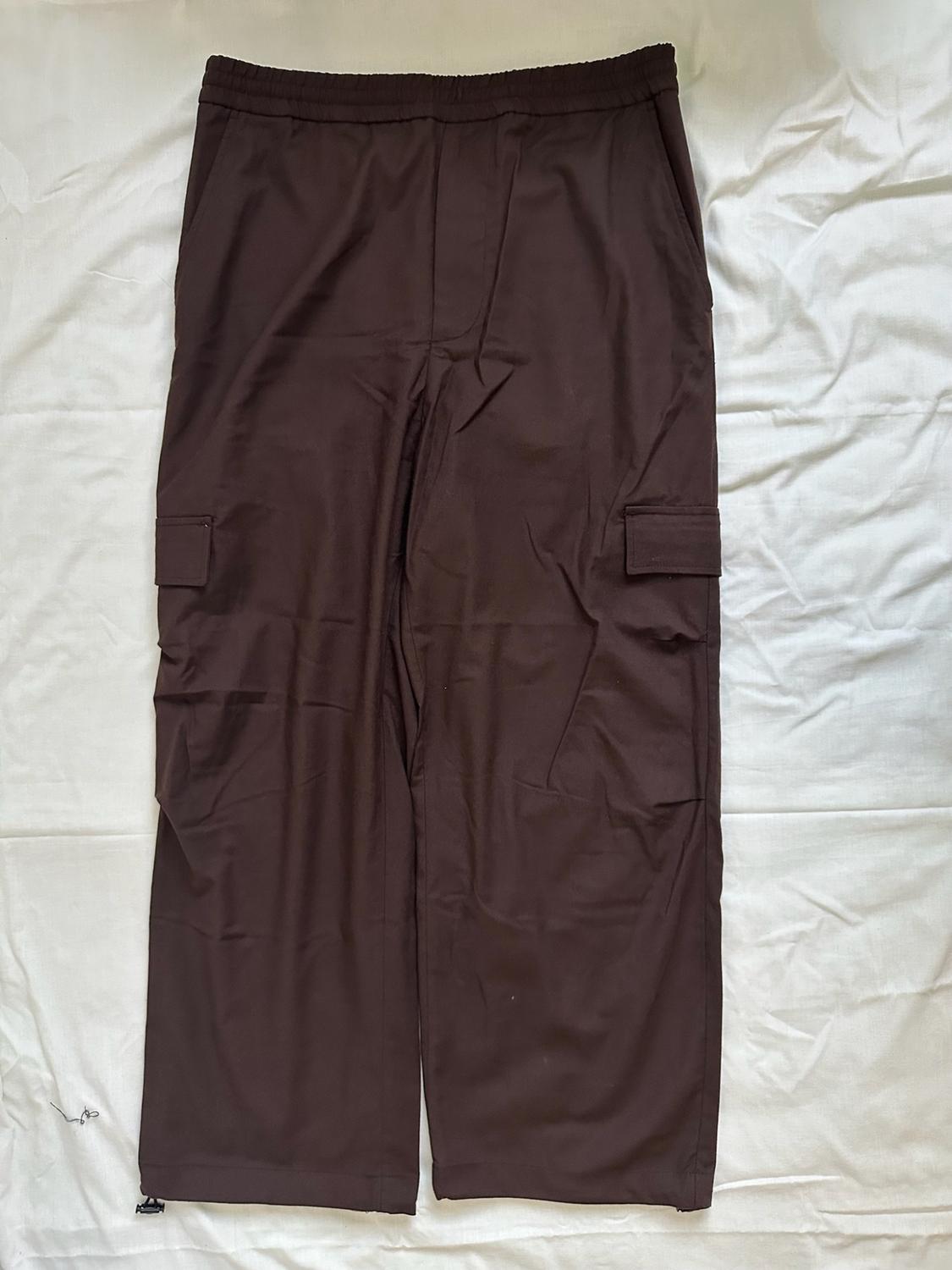 Dark brown wide-leg cargo trousers with an elasticated waist and side pockets, laid out on crumpled white fabric.