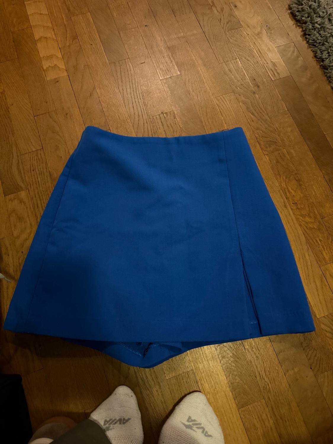 Blue culotte skirt with a slit on a wooden floor. Feet wearing white socks with the text AVIA can be seen below.