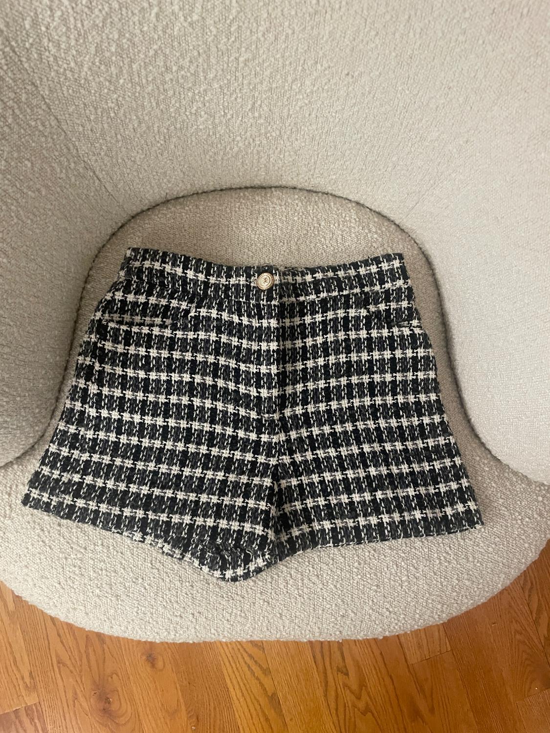 Black and white plaid fabric shorts, placed on a beige chair with visible wooden flooring.
