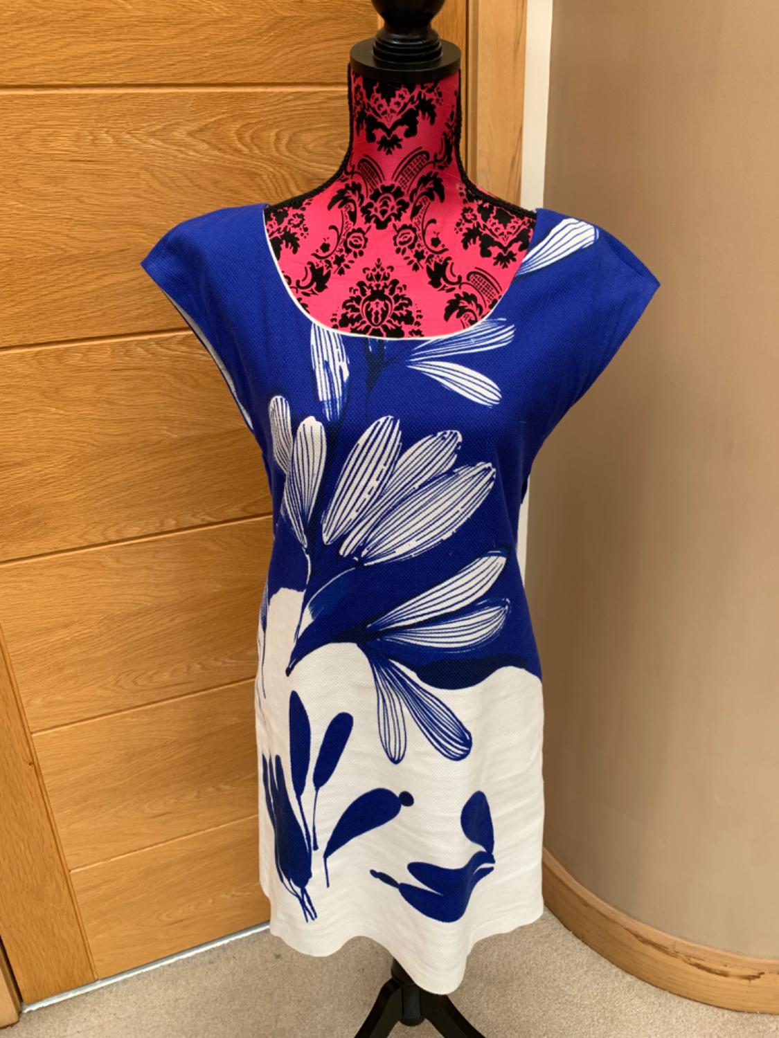 Front view of a blue dress with a white and blue floral print, sleeveless and with a round neck.