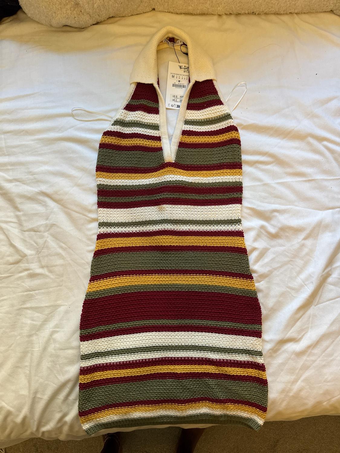 Maroon, green, yellow and white horizontal striped knitted halterneck dress on a bed.