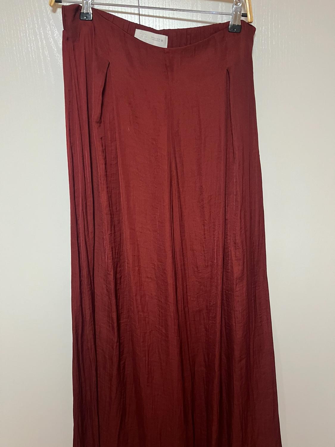 Flowing wide-leg burgundy trousers hanging on a hanger against a white background. ZARA label visible.