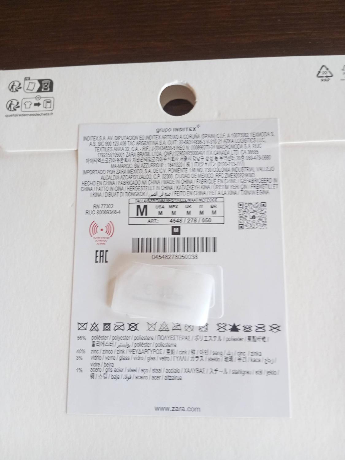 White cardboard label with garment composition and care information. Includes barcode and website: www.zara.com.