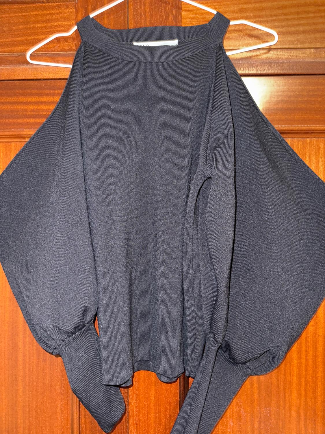 Black long-sleeved off-the-shoulder jumper hanging on a white hanger over a wooden door.