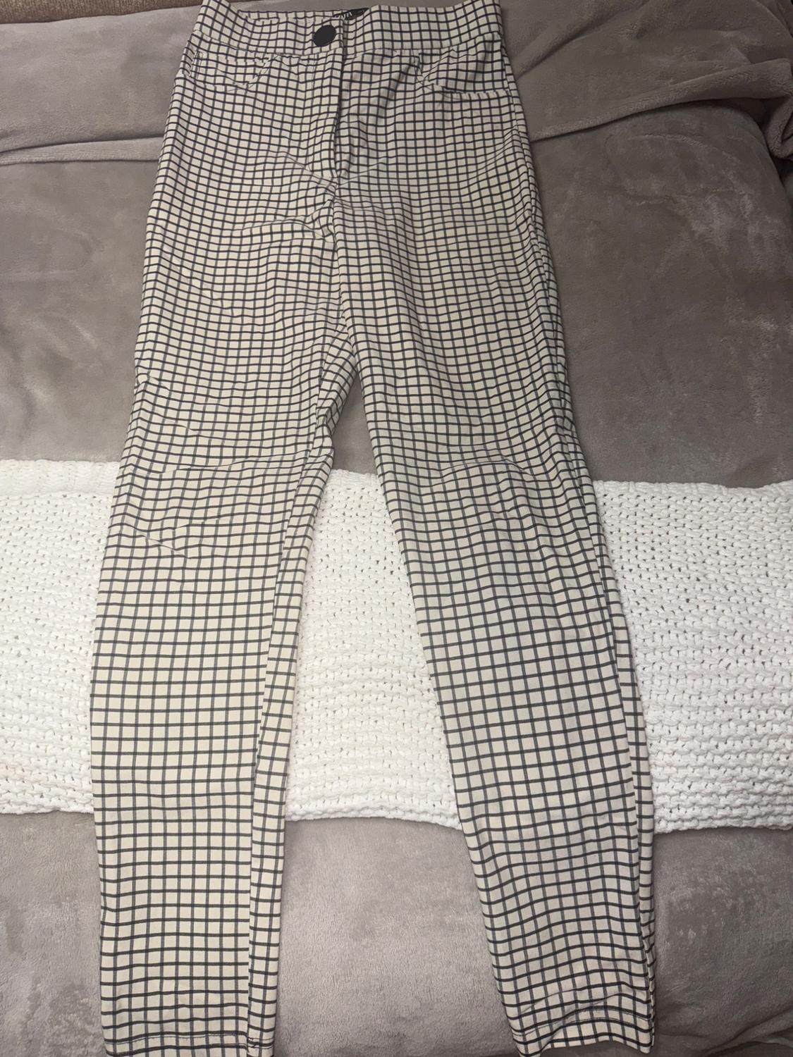 Black and white checkered pants on a gray and white surface. Button and zipper visible at the top.
