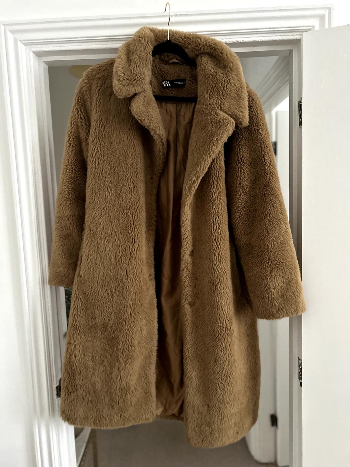 Brown teddy coat hanging on a white door. Visible label with the text "ZARA". Indoor setting.
