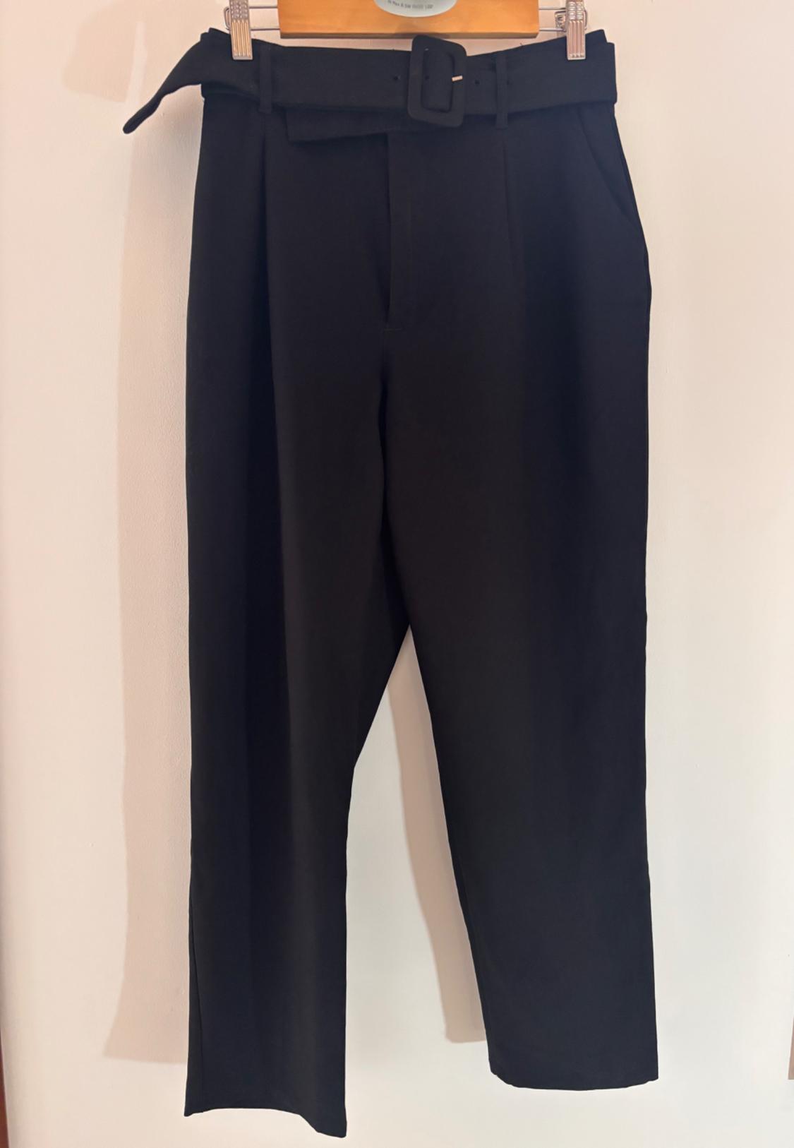 Black trousers hanging on a wooden hanger, with a matching belt and front pleats.