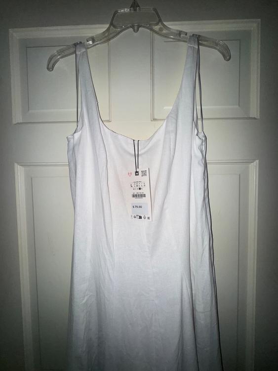 White dress hanging on a clear hanger in front of a white door. Visible tag with a price of $79.90.