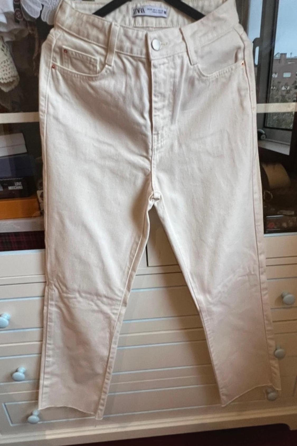 Front view of beige trousers with front pockets and metal button.