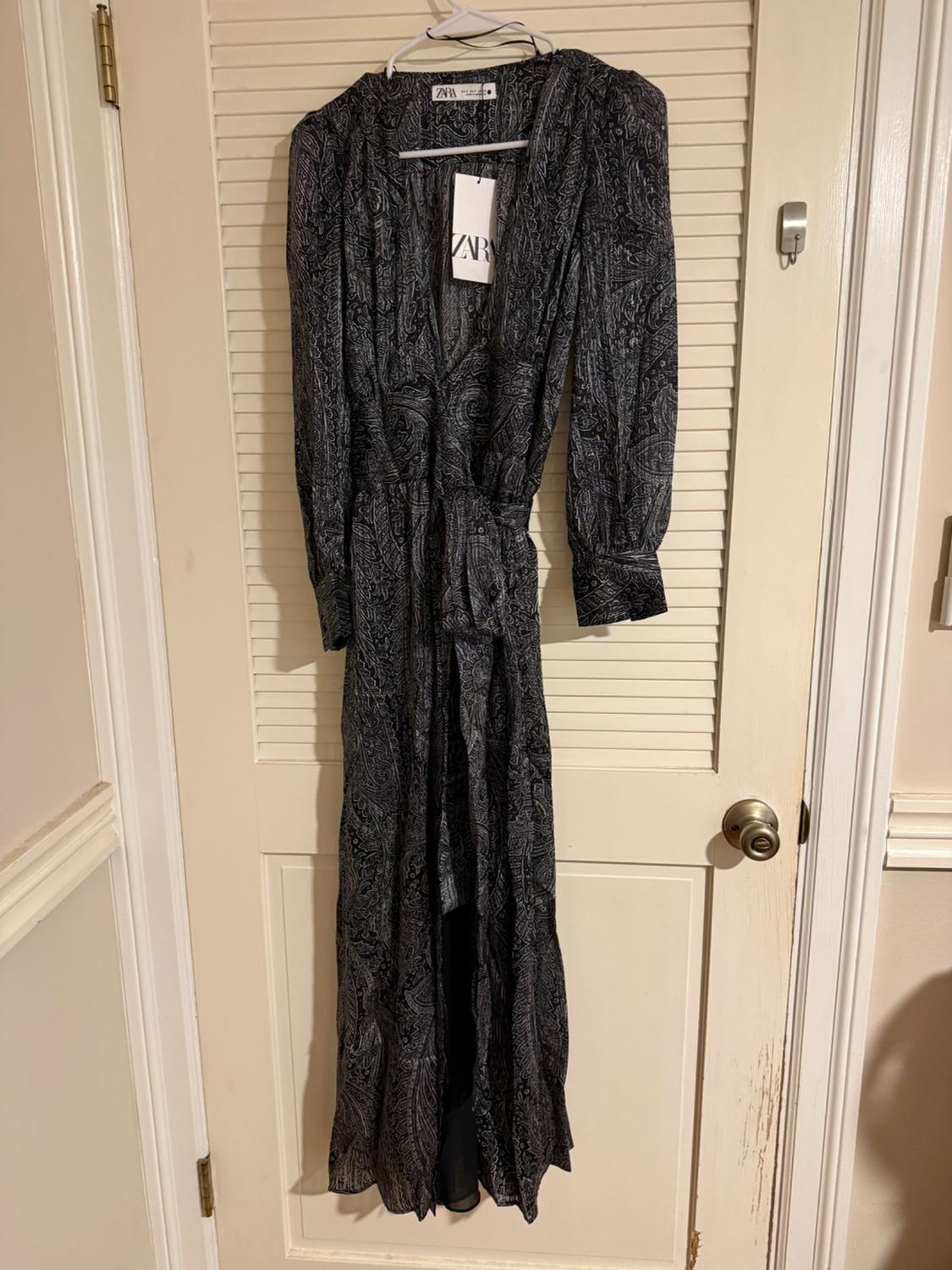 Printed maxi dress in dark tones hanging on a white door. Visible label with the text "ZARA".