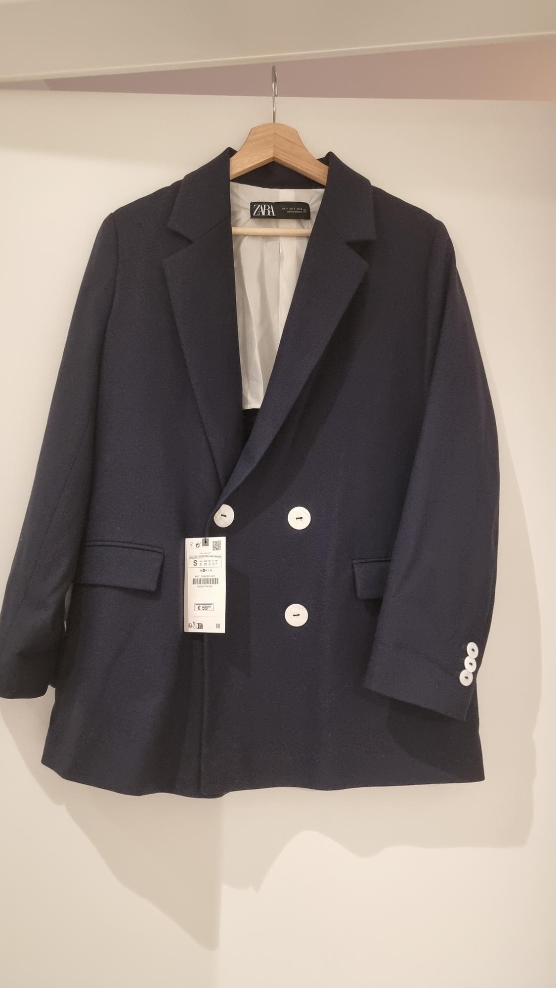 Navy blue double-breasted jacket with white buttons, hanging on a wooden hanger. Visible tag with price of €59.95.