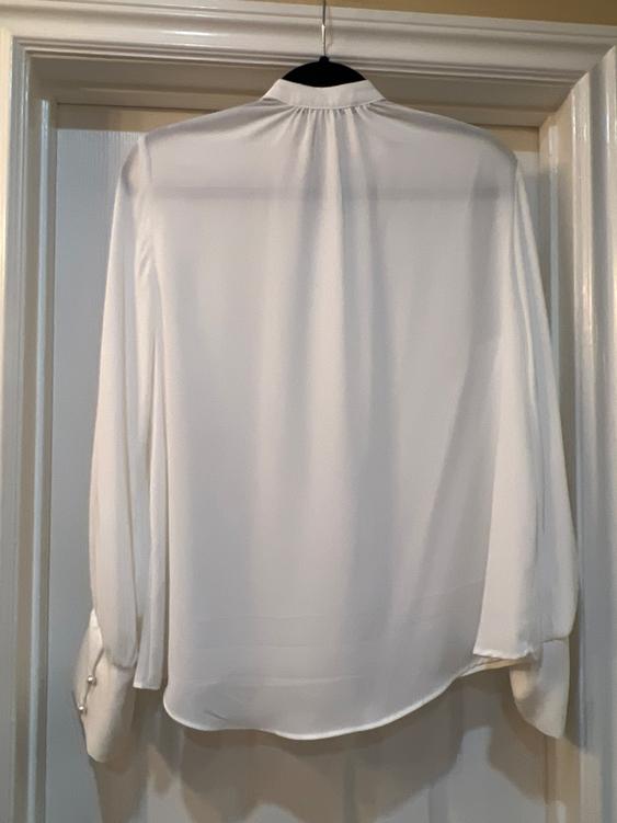 White long-sleeved shirt hanging on a black hanger over a white door. Light fabric and buttons on the cuffs.