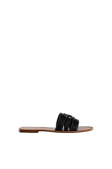 Side view of a black sandal with decorative straps and a flat brown sole.