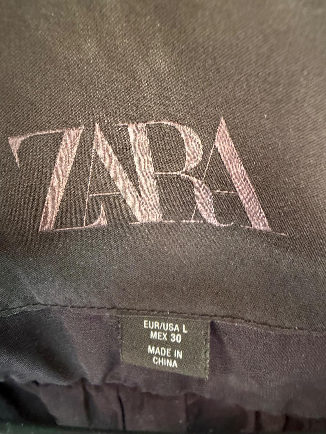 Black clothing label with the text "ZARA" in large. Below, small label: "EUR/USA L, MEX 30, MADE IN CHINA".
