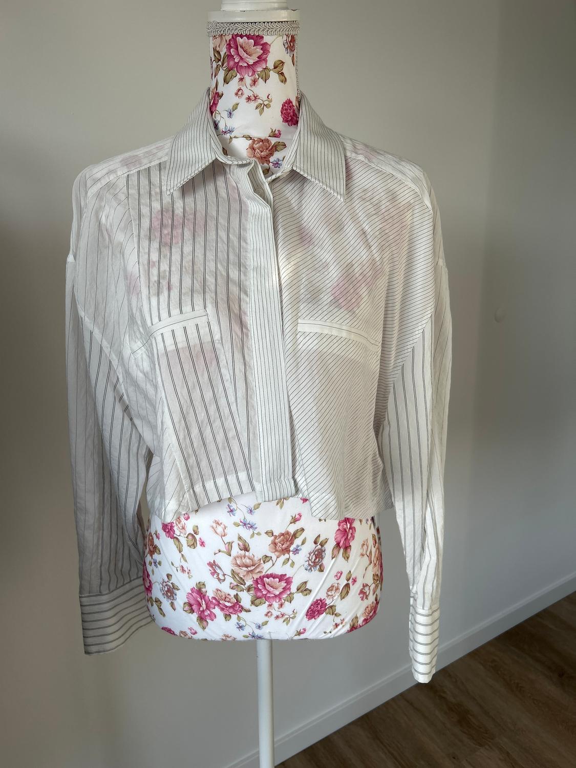 Mannequin in a white shirt with fine vertical stripes, against a floral background. Minimalist setting with a wooden floor.
