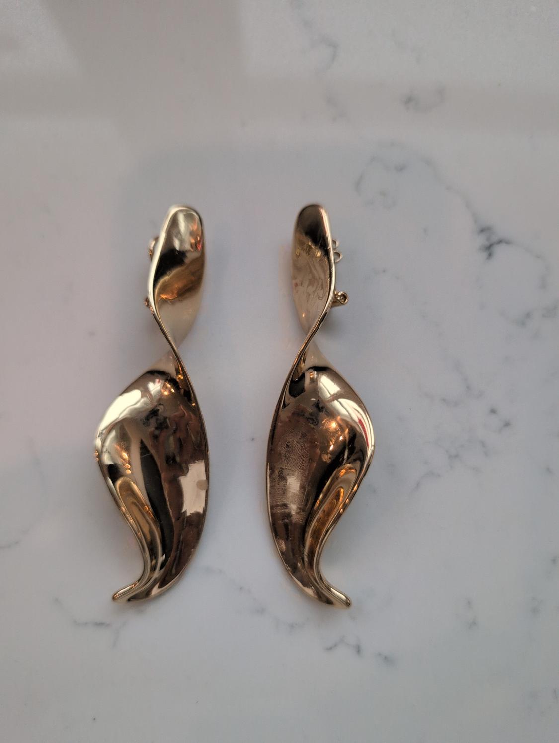 Gold-coloured earrings with a curved and brilliant design on a white marble background.
