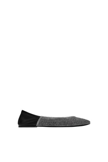 Black flat shoe with a shiny front on a white background. Minimalist and elegant design, ideal for formal occasions.