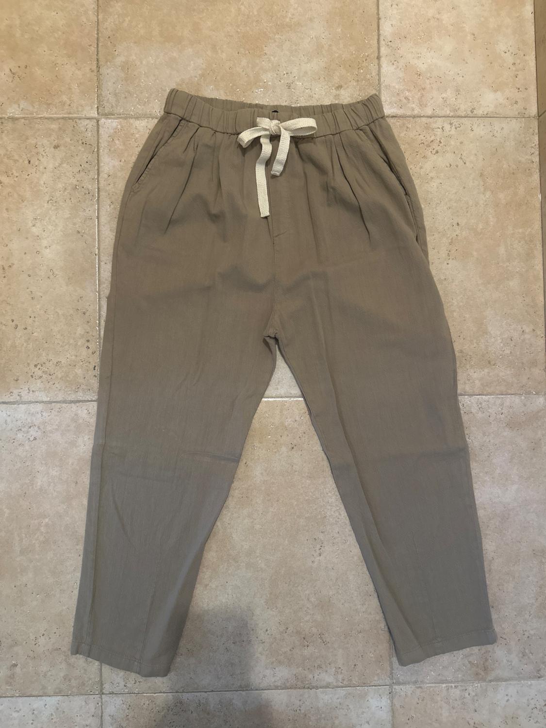 Beige trousers with an elasticated waist and white tie, on a beige tiled floor.
