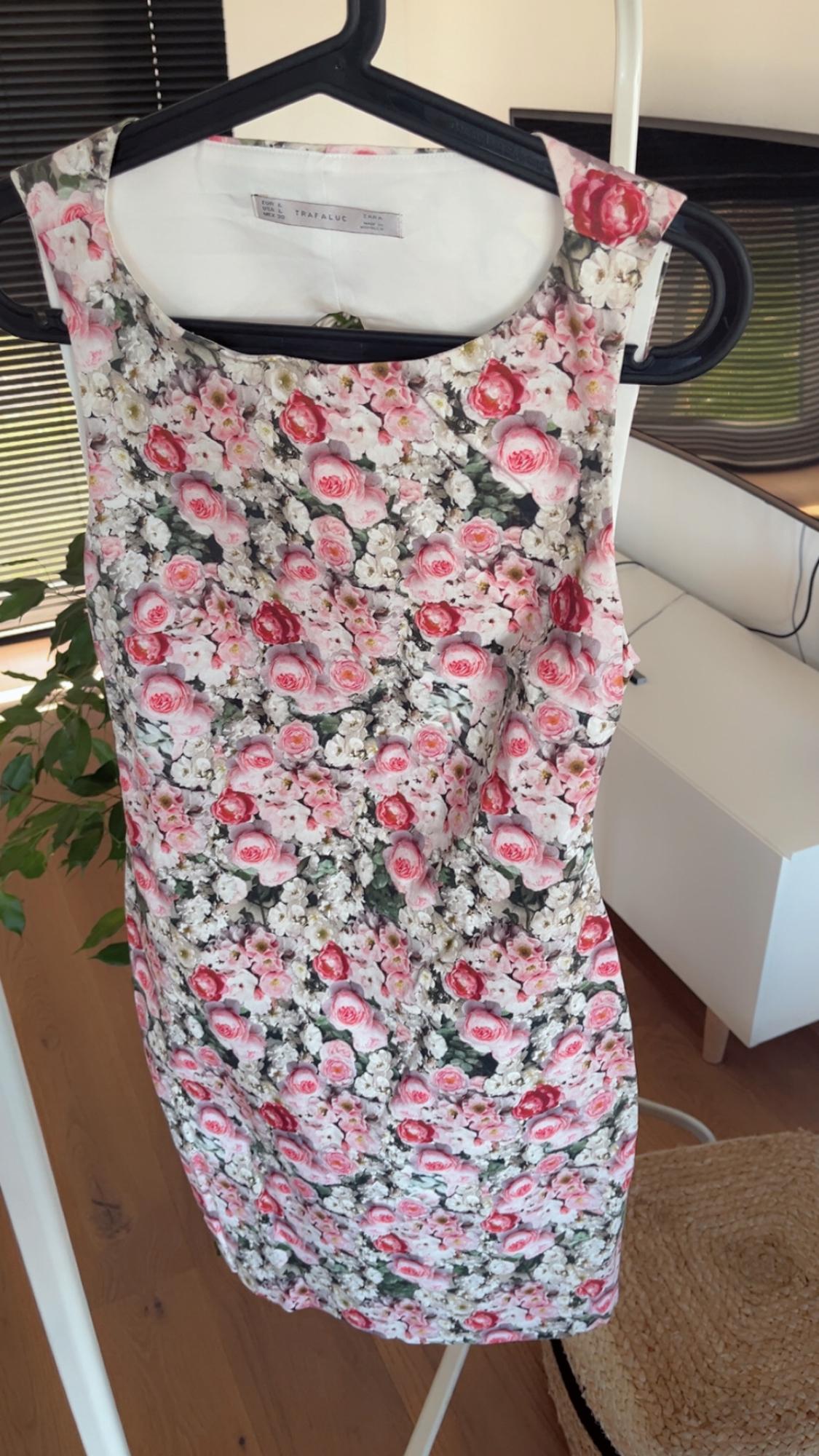 Sleeveless dress with pink and white rose floral print, hanging on a black hanger in a well-lit interior.
