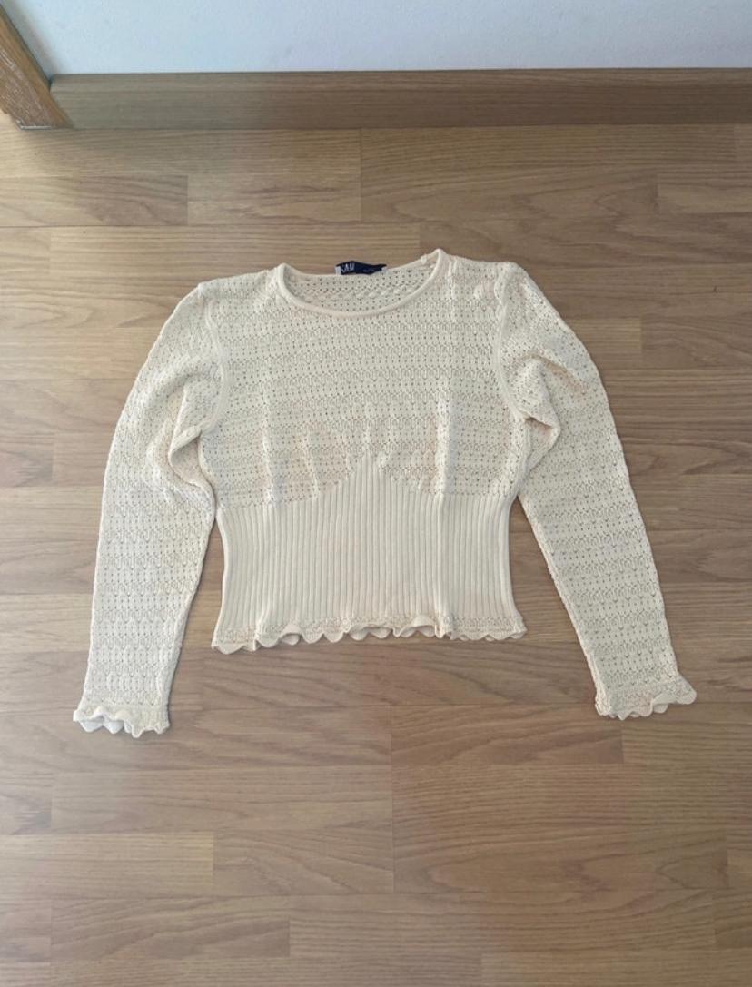 Front view of a long-sleeved beige jumper with a cable knit and a scalloped hem.