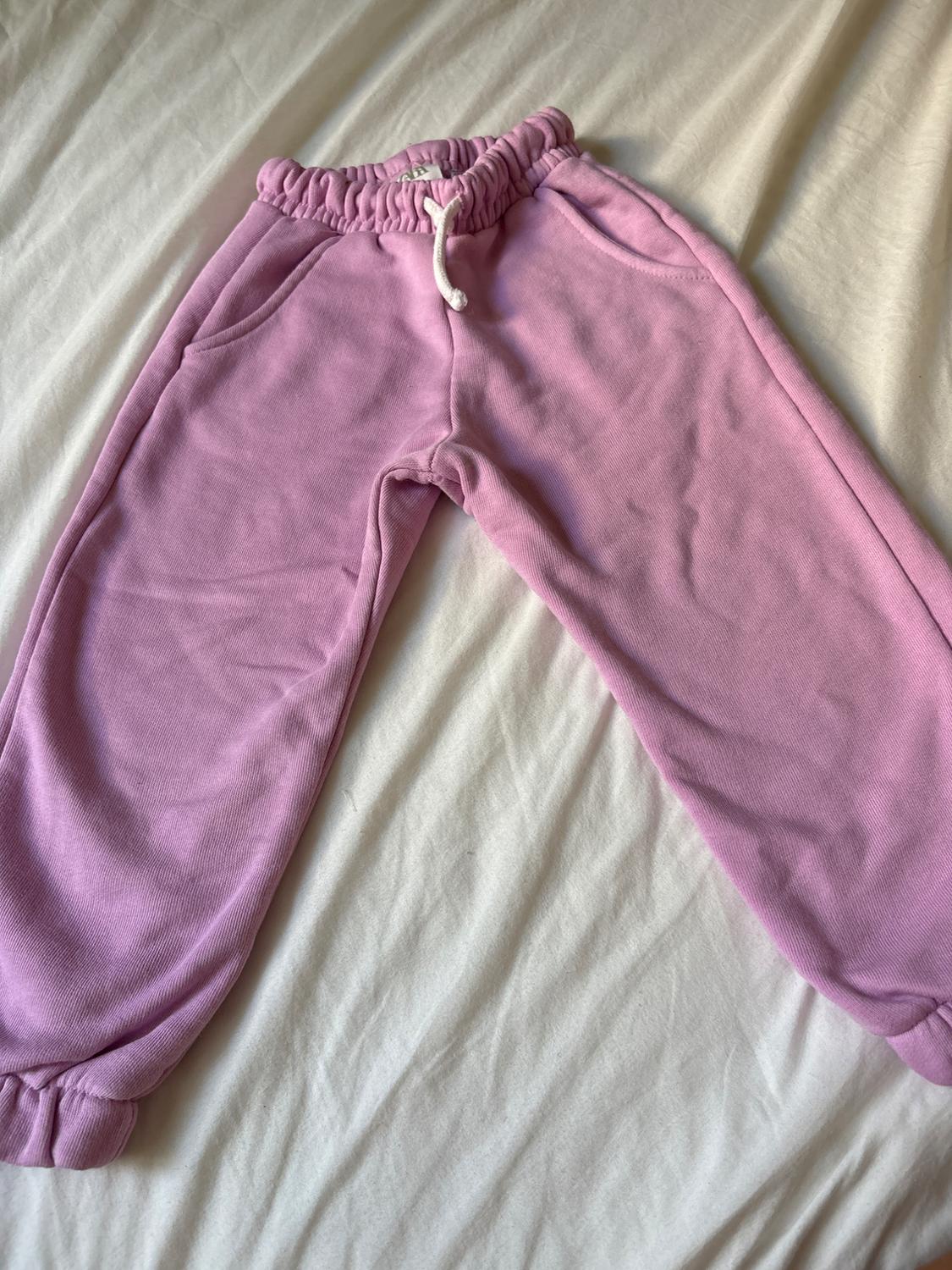 Pink jogging bottoms with an elasticated waistband, white drawstring and side pockets, laid out on a crumpled white sheet.