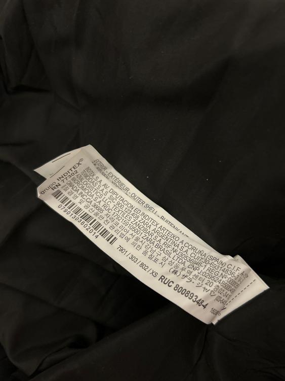 White clothing label with multi-language text on black fabric. Includes manufacturing details and RUC code 800893484.