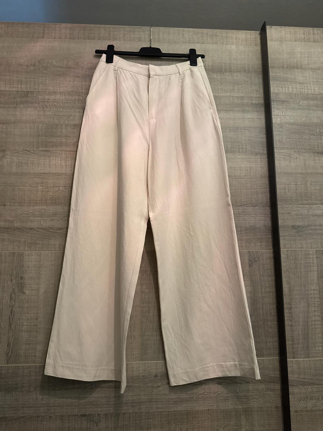 Cream-coloured wide-leg trousers hanging on a black hanger against a wooden wardrobe background. Casual and relaxed style.