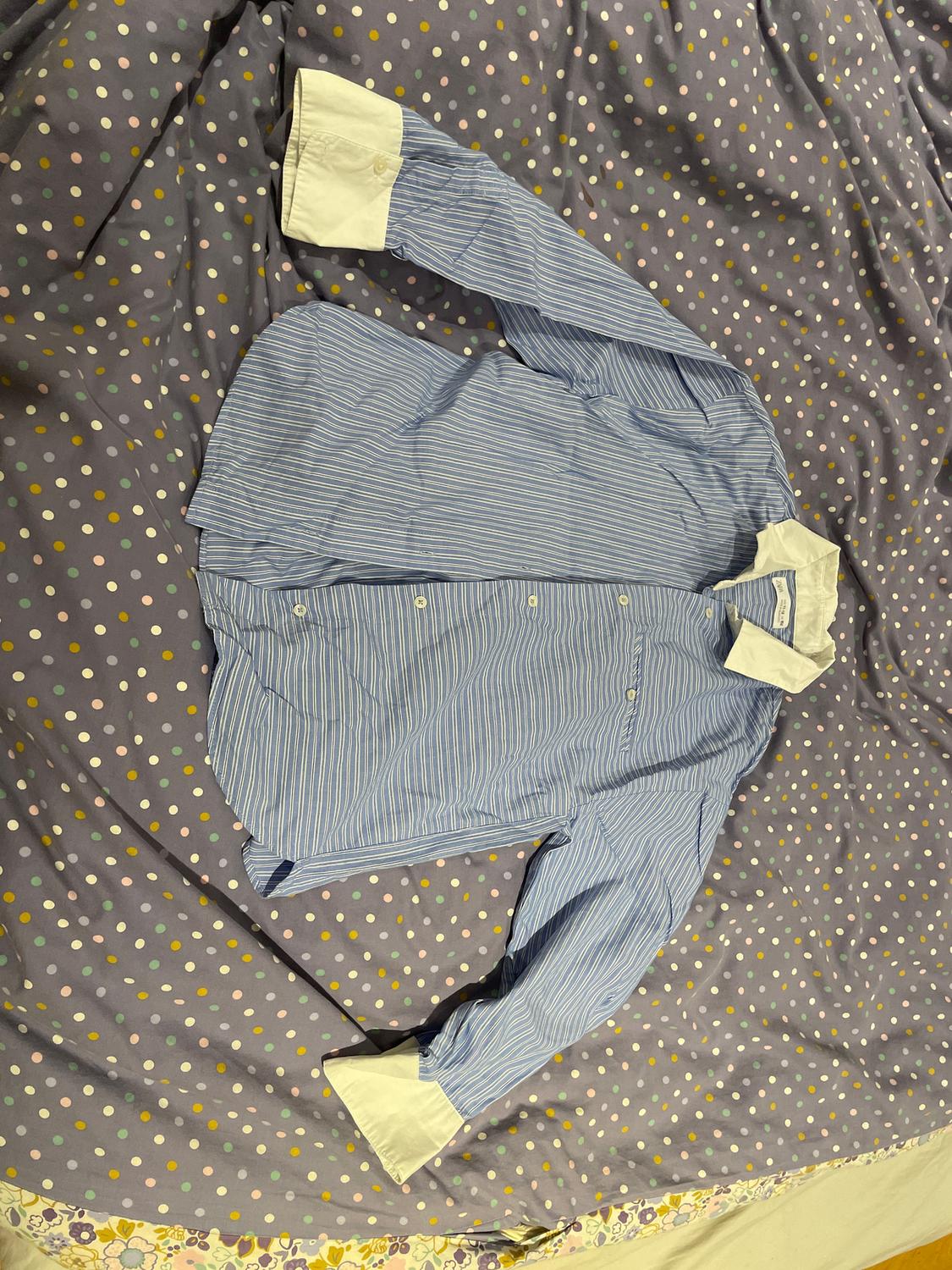 Blue and white striped shirt with white cuffs, placed on a grey duvet with colourful polka dots.
