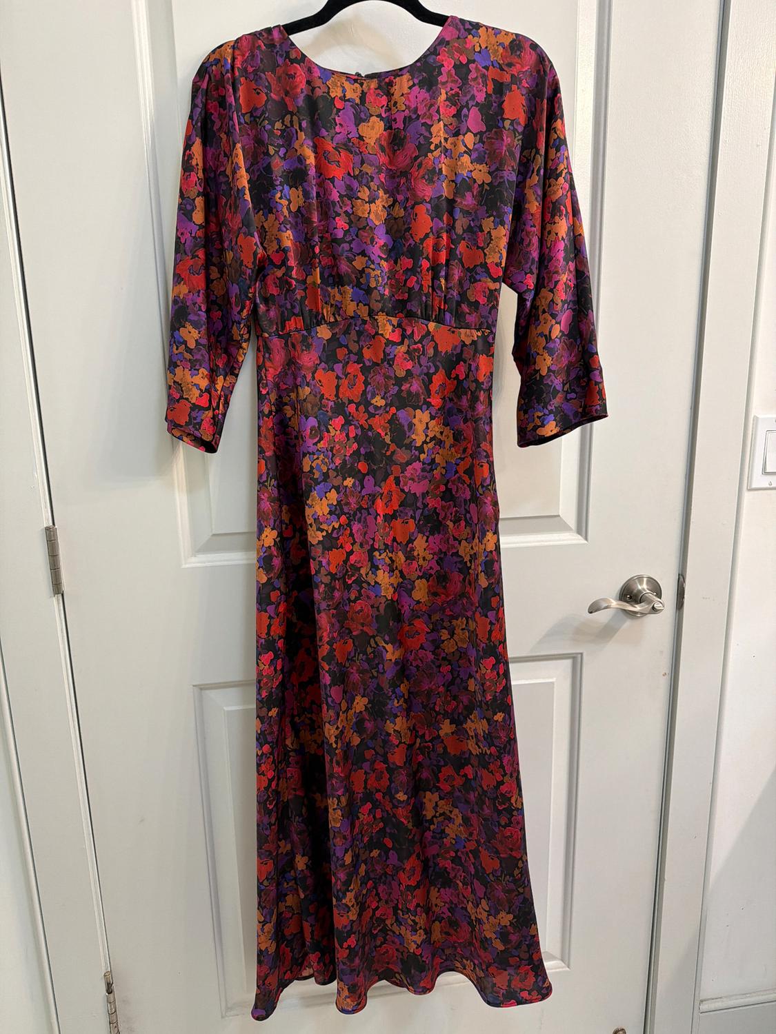 Long dress with a floral print in red, purple, and orange tones, hanging on a hanger over a white door.