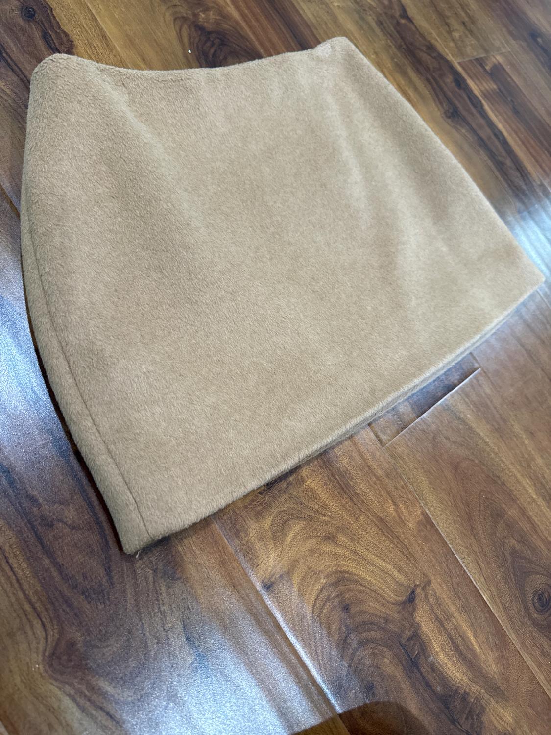 Beige mini skirt on a brown wooden floor. The texture of the skirt is soft, and it looks like it's made of thick fabric.