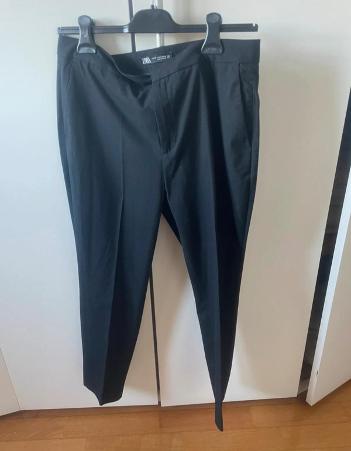 Black trousers hanging on a hanger against a white wardrobe background. The visible label says "Zara".