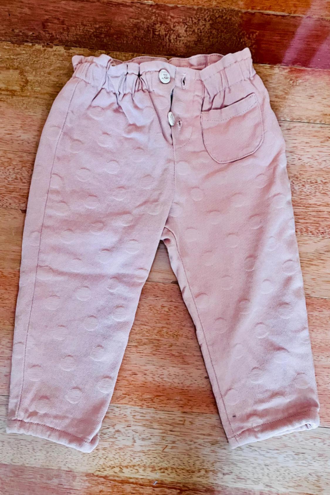 Front view of pink trousers with front pockets and buttons, polka dot texture detail.