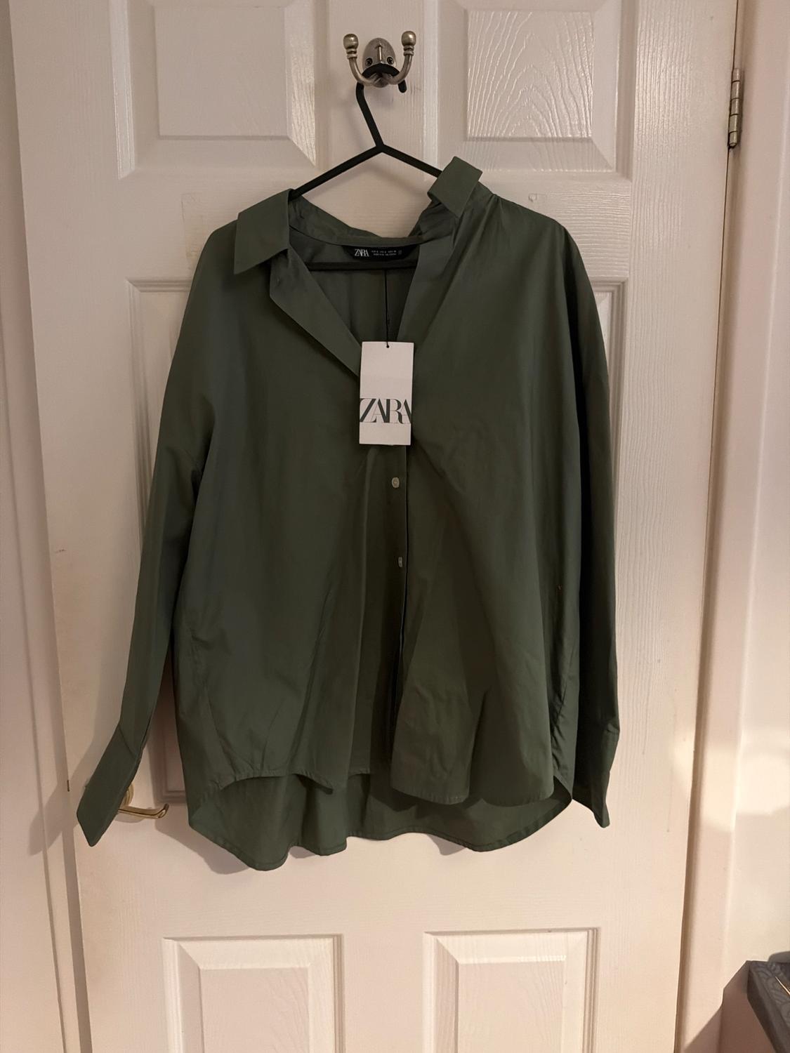 Olive green shirt hanging on a black hanger over a white door. Visible label with the text "ZARA".