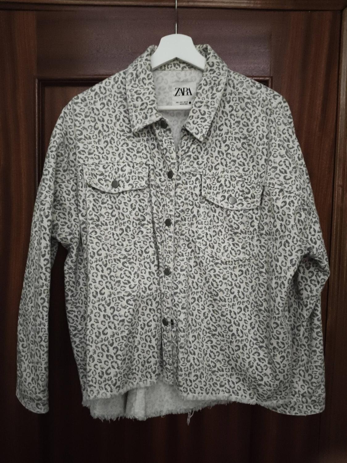 Grey leopard print denim jacket hanging on a white hanger. Visible label with text "ZARA".