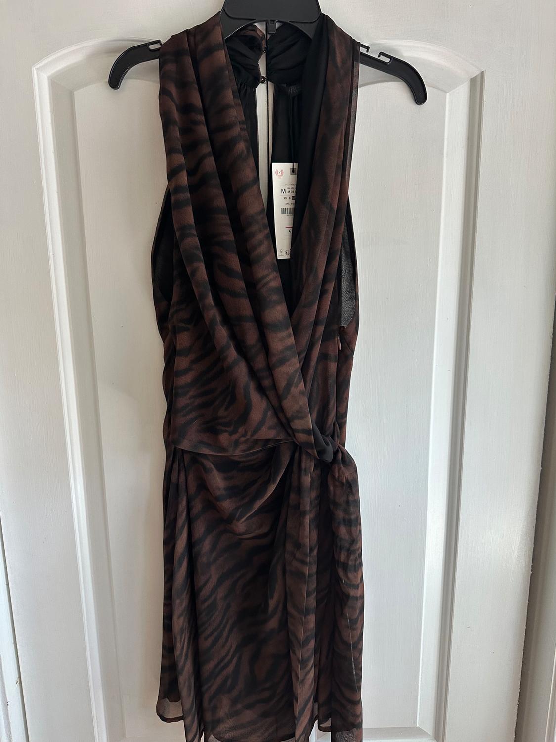 Sleeveless animal print dress in brown and black tones, hanging on a black hanger over a white door.