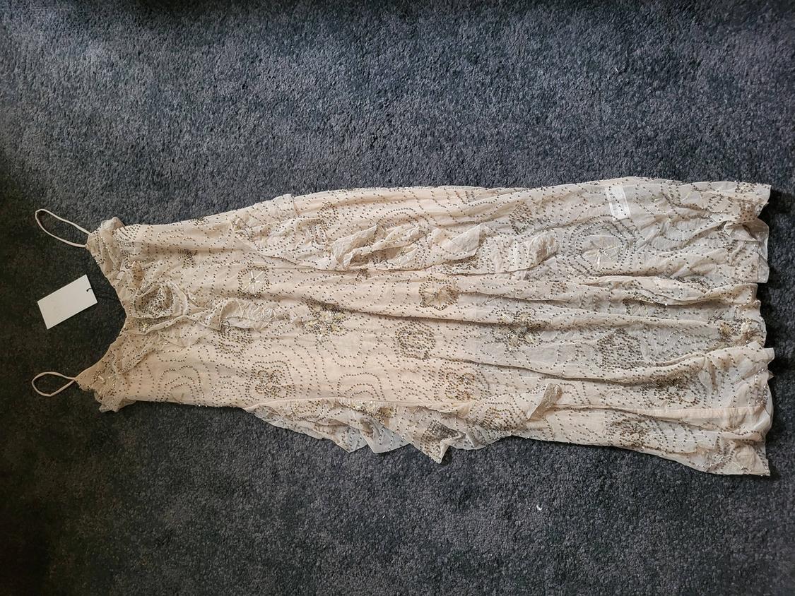 Long beige dress with thin straps and sequin embroidery details on a grey rug. White label visible.