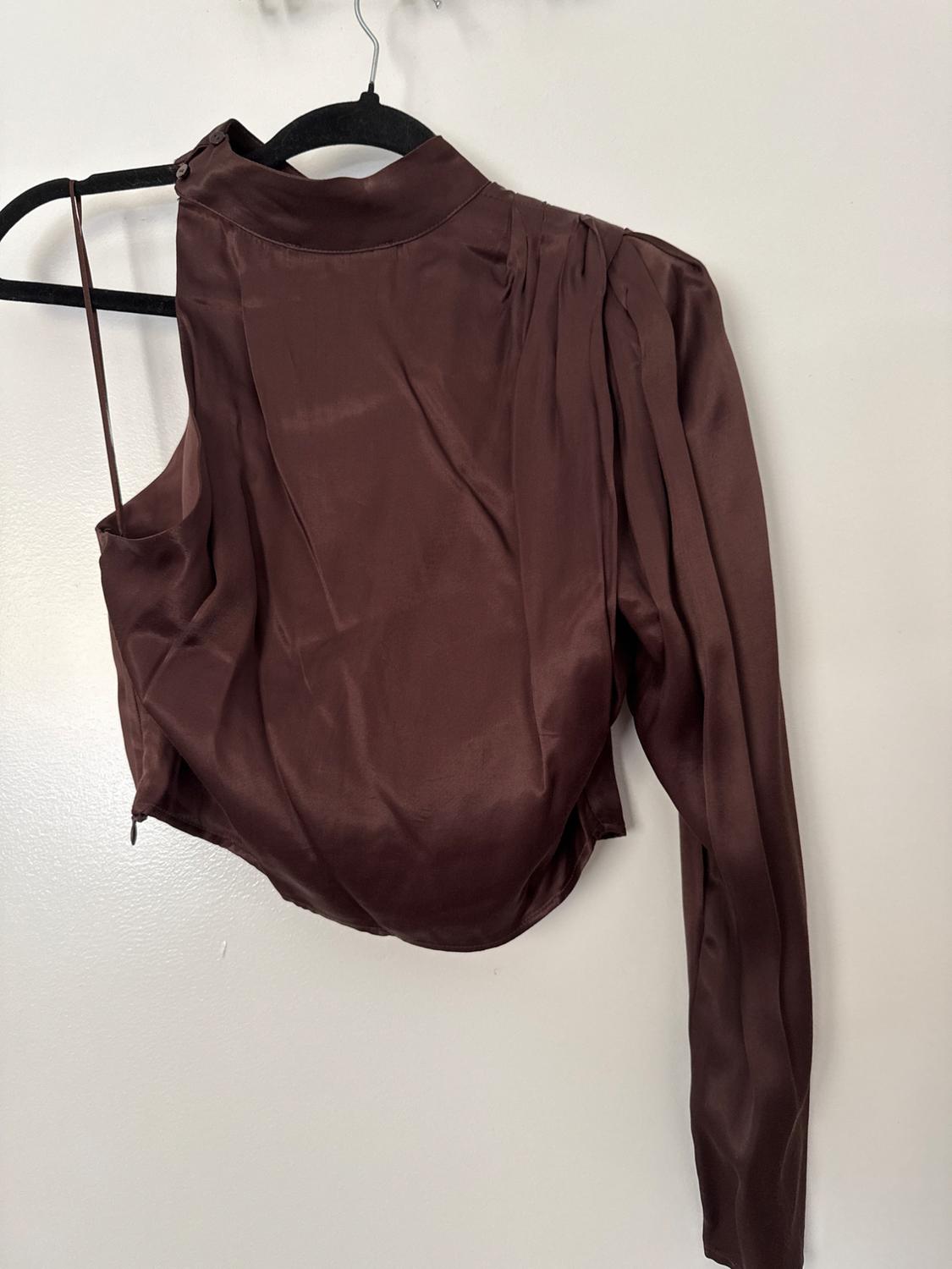 Dark brown asymmetric draped top with a high neck, one long sleeve and one thin strap, hanging on a black hanger against a white wall.