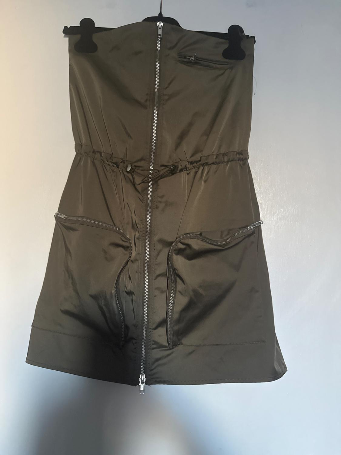 Olive green short dress with front closure and pockets, hanging on a black hanger on a white background.