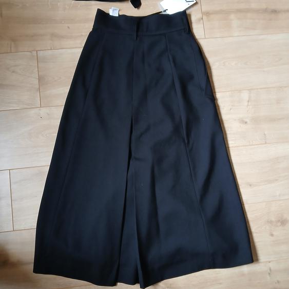 Black high-waisted culottes on light wooden flooring. Visible label at the waist.
