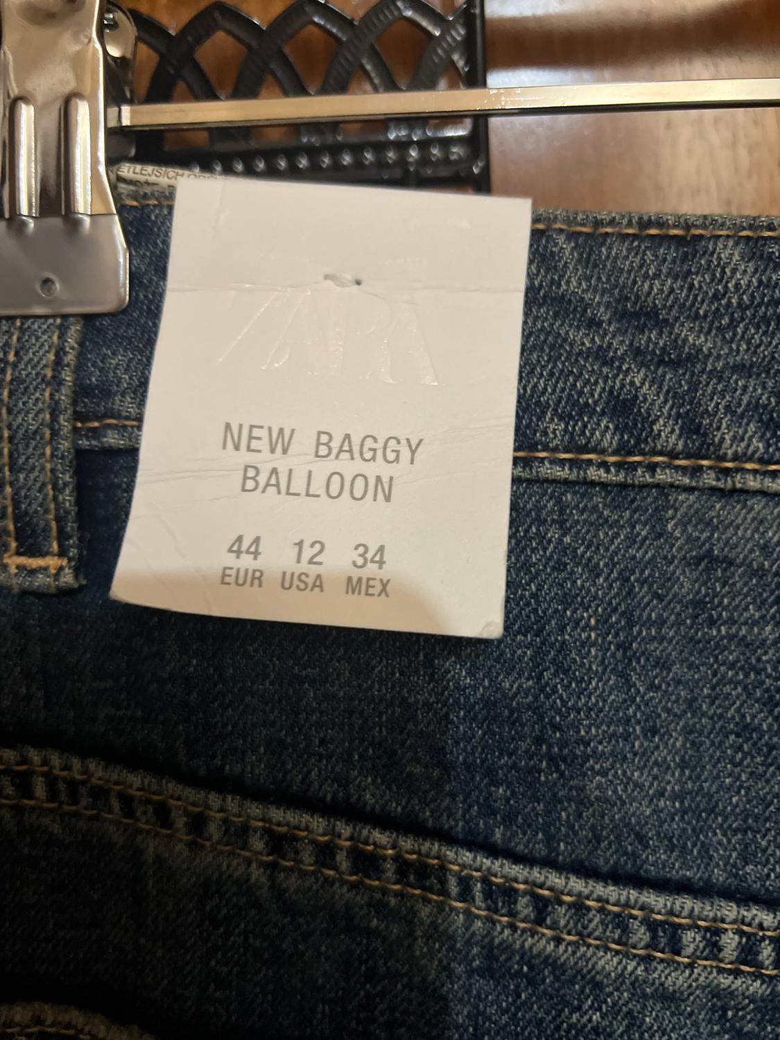 Close-up of blue jeans on a hanger. The white label reads: ZARA NEW BAGGY BALLOON 44 12 34 EUR USA MEX.