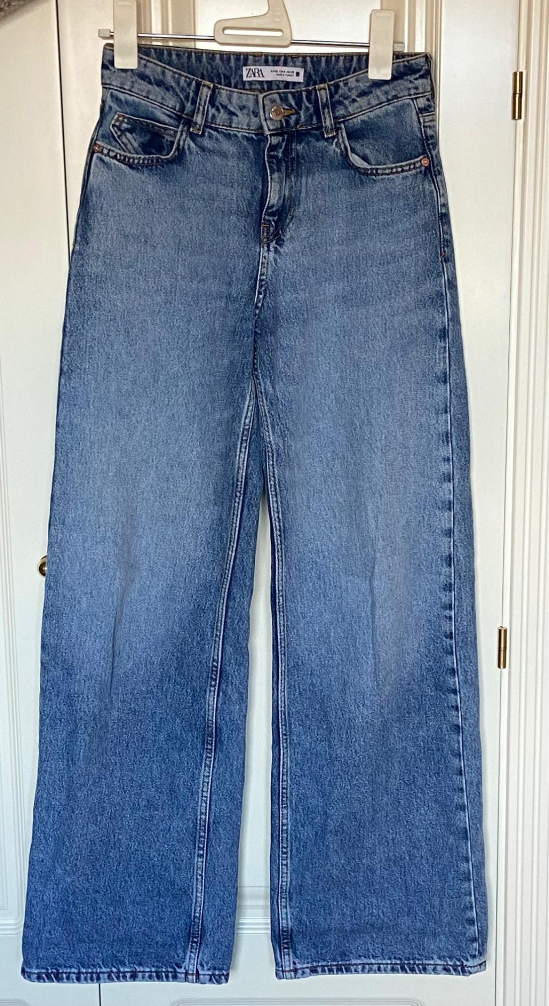 Blue wide-leg jeans hanging on a white hanger, with a visible Zara label on the waistband.